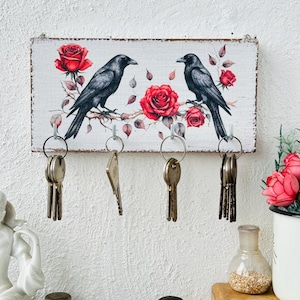 May include: White wooden key holder with a distressed finish. The key holder features a painted design of two black crows perched on a branch with red roses. There are five key hooks.