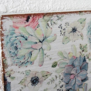 May include: A wooden wall-mounted key holder with a floral design featuring succulents and anemones in shades of pink, blue, and green. The wood has a distressed white finish.