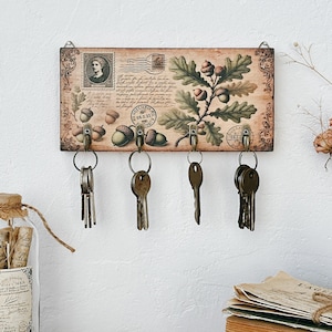 Könnte beinhalten: Ein Schlüsselhalter aus Holz mit einem Vintage-Design mit einem Eichenblatt und Eicheln. Der Halter hat fünf Haken zum Aufhängen von Schlüsseln. Der Text "GRECILIORI" ist auf dem Halter aufgedruckt.