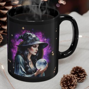 May include: Black coffee mug with a colorful illustration of a witch holding a crystal ball. The witch is wearing a black hat with a white and black checkered pattern. The background is a purple and pink galaxy with stars.