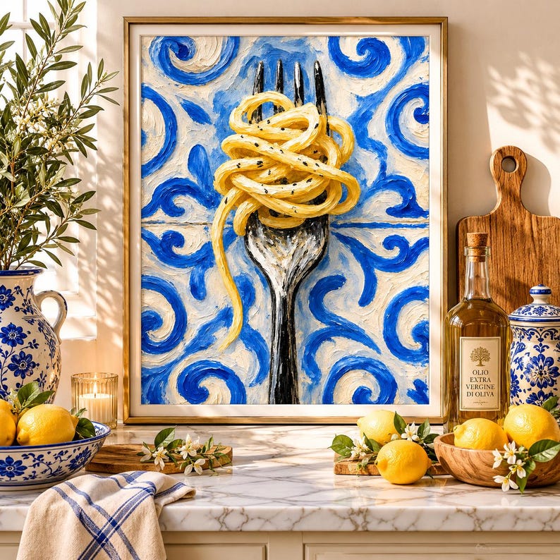 May include: A framed oil painting depicting a silver fork twirling yellow spaghetti with black pepper specks, set against a blue and white swirling tile pattern. The artwork is displayed on a kitchen counter with lemons and olive oil.
