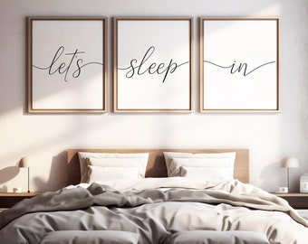 Puede incluir: Tres impresiones enmarcadas con el texto "let's sleep in" en un ambiente de dormitorio moderno. Las impresiones están colgadas sobre una cama con ropa de cama blanca y una cabecera de madera.