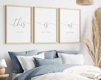 May include: Three framed prints with the text "this is us" and the words "our life", "our story", and "our home" underneath each word. The prints are hanging on a white wall above a bed with blue bedding.