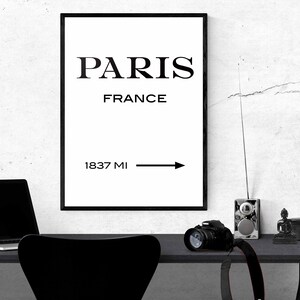 Op de afbeelding: Zwart-witte print met de tekst "PARIS FRANCE 1837 MI" en een pijl die naar rechts wijst. De print is ingelijst en hangt aan een witte muur.