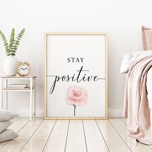 May include: A framed print with a gold frame and a white background. The print features a pink watercolor rose and the text "STAY POSITIVE" in black cursive font.