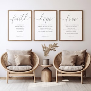 Puede incluir: Tres impresiones enmarcadas con las palabras "fe", "esperanza" y "amor" en una fuente de caligrafía moderna. Cada impresión incluye un versículo bíblico relacionado con la palabra. Las impresiones están colgadas en una pared blanca sobre dos sillas de mimbre.