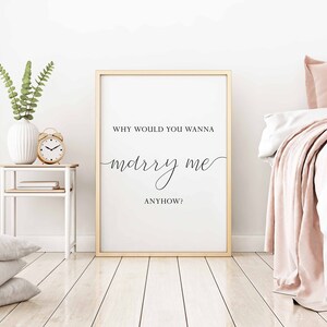 Puede incluir: Una impresi&oacute;n enmarcada en blanco con el texto "Why would you wanna marry me anyhow?" en fuente cursiva negra. La impresi&oacute;n est&aacute; colgada en una pared blanca en un dormitorio.