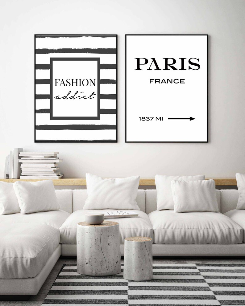 Op de afbeelding: Twee zwart-witte ingelijste prints met een minimalistisch ontwerp. De linker print heeft zwart-witte strepen met de tekst "FASHION addict" in een zwarte doos. De rechter print heeft de tekst "PARIS FRANCE" met een pijl die naar rechts wijst en de tekst "1837 MI" eronder.