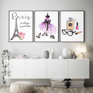 May include: Three framed watercolor prints with a Parisian theme. The first print features a black and white illustration of the Eiffel Tower with pink flowers. The second print features a purple dress with a black bow and black shoes. The third print features a bottle of perfume, a pair of glasses, a lipstick, and a nail polish bottle.