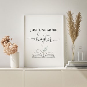 May include: A printable wall art design with the text "Just one more chapter" in black script font. An open book with a green leaf is illustrated below the text.