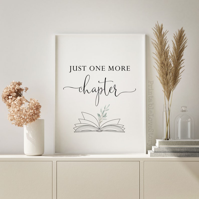 May include: A printable wall art design with the text "Just one more chapter" in black script font. An open book with a green leaf is illustrated below the text.