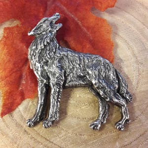 May include: A silver-coloured pewter wolf figurine with a detailed, textured surface. The wolf is standing on all four legs with its head tilted back and mouth open, as if howling.