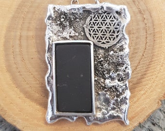 May include: A silver necklace with a rectangular pendant featuring a black stone and a silver flower of life design.