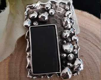 May include: A silver pendant featuring a black stone set within a textured frame. The frame is adorned with small, round silver beads.