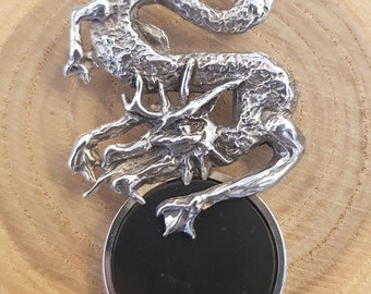 May include: A silver dragon pendant featuring a black onyx stone. The dragon is curled around the stone, with its wings outstretched. The pendant is on a silver chain.