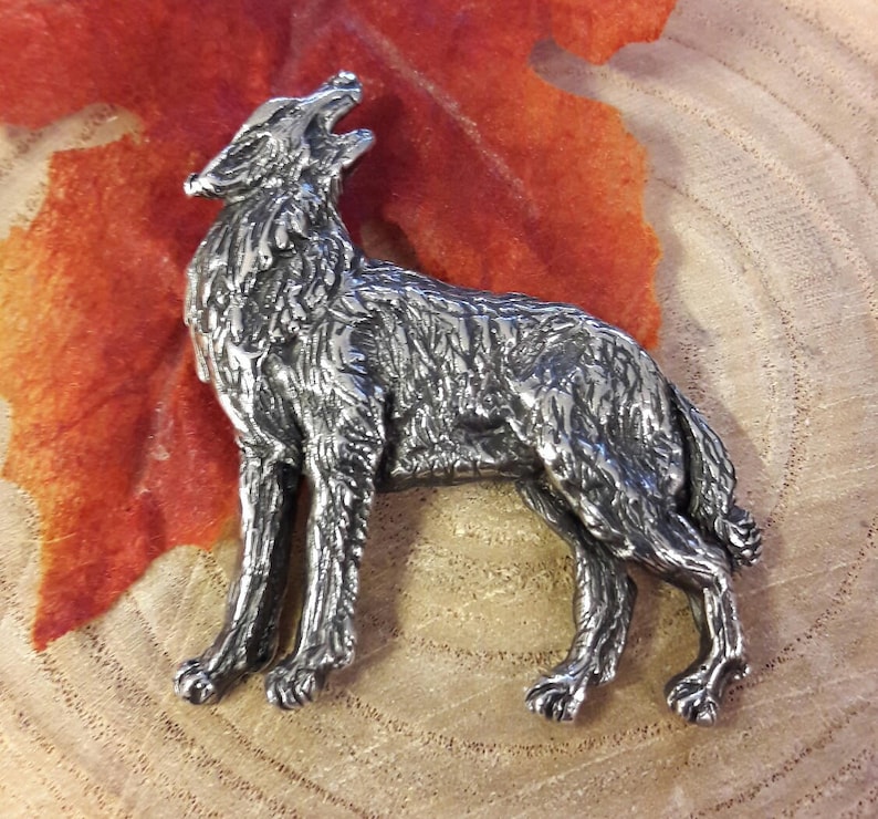 May include: A silver-coloured pewter wolf figurine with a detailed, textured surface. The wolf is standing on all four legs with its head tilted back and mouth open, as if howling.