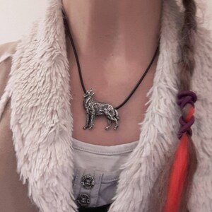 May include: A silver wolf pendant necklace on a black cord. The pendant is detailed and realistic, with the wolf howling at the moon.