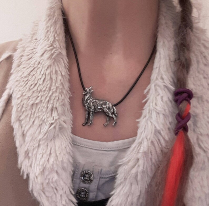 May include: A silver wolf pendant necklace on a black cord. The pendant is detailed and realistic, with the wolf howling at the moon.
