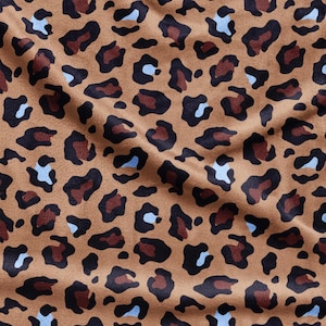 May include: A fabric featuring a repeating leopard print pattern on a tan background. The design consists of irregular black outlines filled with dark brown centers and small, light blue accents scattered throughout the textured material surface.