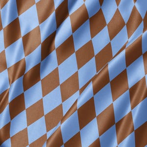 May include: A fabric with a repeating diamond pattern in alternating light blue and brown colors. The material has a smooth, slightly reflective surface with soft folds that create subtle shadows and highlights across the geometric design.
