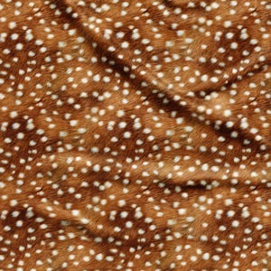 Op de afbeelding: Een stof met een bruine basiskleur en een herhalend patroon van kleine, onregelmatige witte stippen. Het materiaal heeft een getextureerd, bontachtig uiterlijk met zichtbare plooien en draperingen die subtiele schaduwen op het oppervlak werpen.
