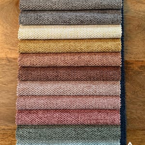 Peut inclure: Un nuancier de tissus présentant une variété d'échantillons de revêtements texturés dans des tons de beige, de gris, d'or et de rose. Les échantillons sont disposés en pile verticale, présentant les différentes options de couleurs. Le texte "EASY CLEAN" est également visible.