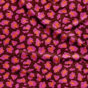 Peut inclure: Un tissu présentant un motif léopard répétitif avec un fond marron foncé, des taches rose vif et des centres orange éclatant. Le matériau présente des plis et des ondulations souples qui créent un aspect texturé sur toute la surface.