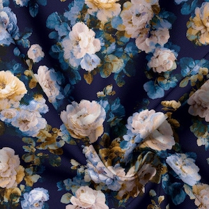 May include: A dark navy blue fabric featuring a dense floral pattern of cream, pale yellow, and light blue roses with green leaves. The material has a visible woven texture and is folded to create soft shadows across the floral print design.