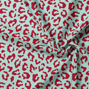 May include: A fabric featuring a repeating leopard print pattern with dark red, irregular, organic-shaped spots set against a solid light mint green background. The material displays soft folds and gathers, highlighting the texture of the textile.