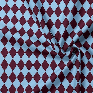 Könnte beinhalten: Ein Stoff mit einem sich wiederholenden Argyle-Muster aus hellblauen und dunkelweinroten Rauten. Das Material ist in weichen Falten und Raffungen dargestellt, die das geometrische Design und die Webstruktur des Textils hervorheben.