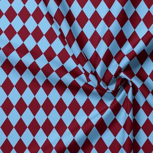 May include: A fabric featuring a repeating argyle pattern of alternating light blue and deep maroon diamonds. The material is shown with soft folds and drapes, highlighting the geometric design and the consistent texture of the textile surface.