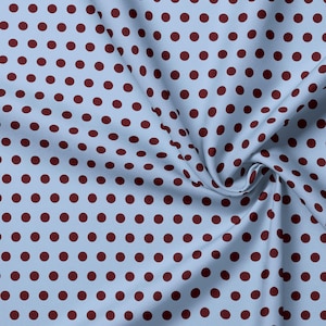 Pode incluir: Um tecido azul-claro com um padrão repetitivo de bolinhas em tom bordô escuro. O material apresenta uma textura tecida visível e está franzido numa dobra suave no lado direito, criando sombras naturais e profundidade na superfície.