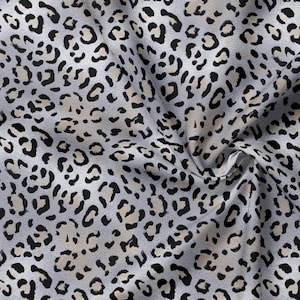 May include: A fabric featuring a repeating leopard print pattern in shades of light gray, beige, and black. The material is shown with soft folds and drapes, highlighting the texture of the textile and the consistent distribution of the animal spots.