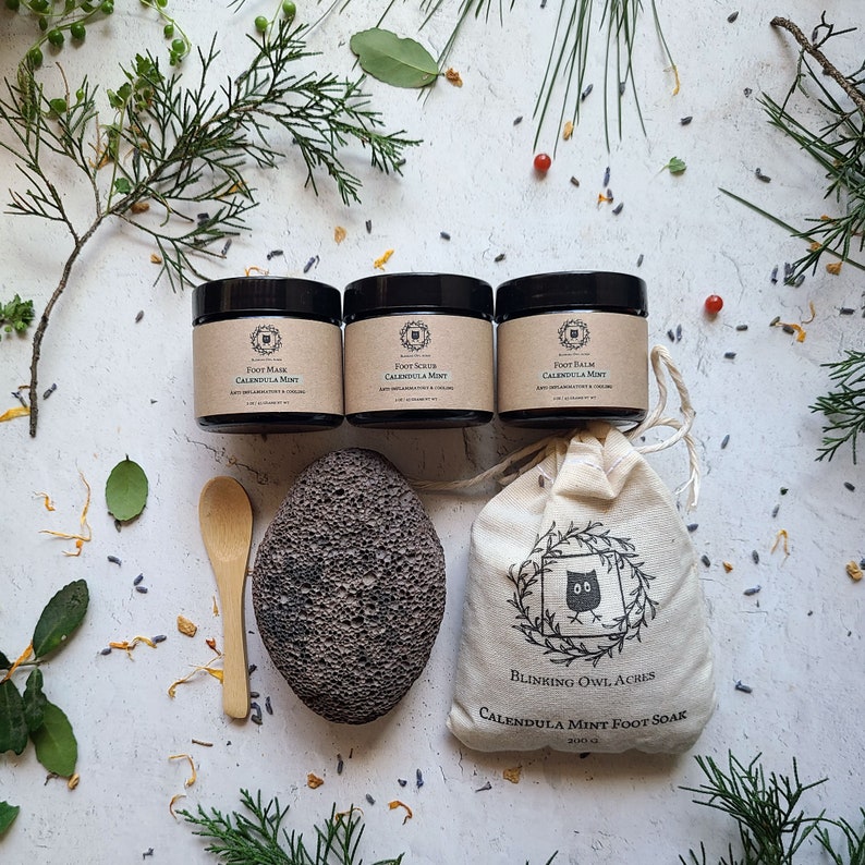 Foot Mask Jar, Foot Scrub Jar, Foot Balm Jar, Bamboo Scoop Spoon, Large Lava Pumice stone, Foot Soak Bag. Plaster background with botanical elements scattered
