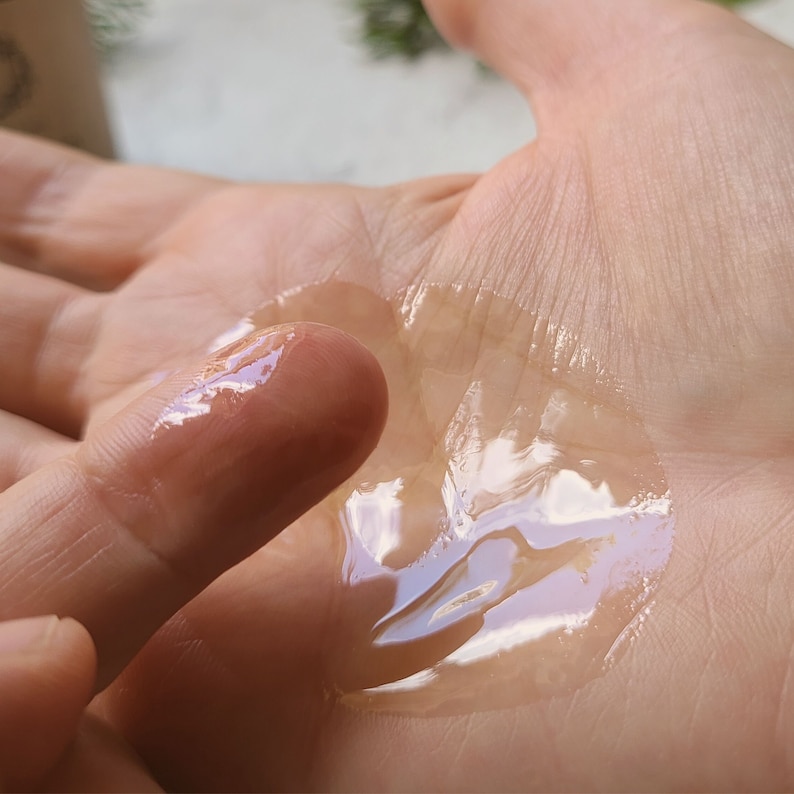 May include: A clear, viscous liquid is spread on a person's hand. The liquid is thick and has a slight sheen. The liquid is being spread with a finger.