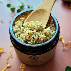 Pu&ograve; includere: Primo piano di un barattolo di vetro pieno di uno scrub per i piedi verde e bianco a base di zucchero. Un cucchiaio di legno sta prelevando lo scrub. Il barattolo ha un'etichetta che recita "Scrub per i piedi Eucalipto e Menta".