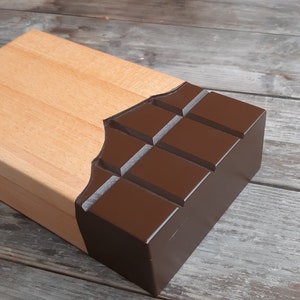 Puede incluir: Una caja de madera con un dise&ntilde;o de barra de chocolate. La caja est&aacute; hecha de madera clara y tiene un dise&ntilde;o de barra de chocolate marr&oacute;n oscuro en la parte delantera. La barra de chocolate est&aacute; dividida en cuadrados y tiene un acabado brillante.