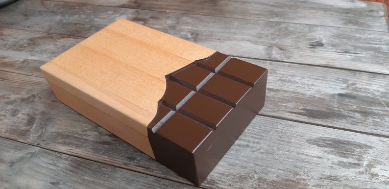 Puede incluir: Una caja de madera con un dise&ntilde;o de barra de chocolate. La caja est&aacute; hecha de madera clara y tiene un dise&ntilde;o de barra de chocolate marr&oacute;n oscuro en la parte delantera. La barra de chocolate est&aacute; dividida en cuadrados y tiene un acabado brillante.