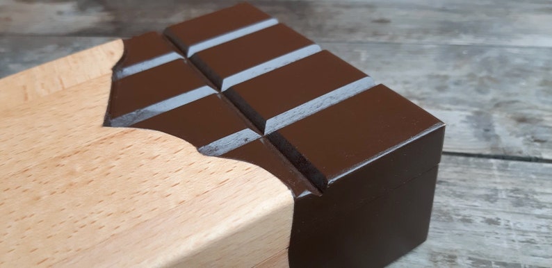 Puede incluir: Una caja de madera con forma de barra de chocolate con la parte superior pintada de marr&oacute;n y la base de madera natural.