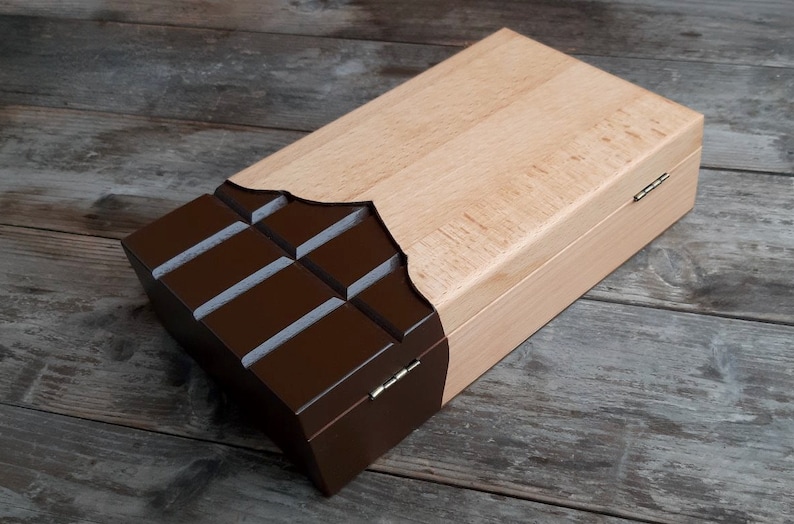 Puede incluir: Una caja de madera con un dise&ntilde;o de barra de chocolate. La caja est&aacute; hecha de madera clara y tiene un dise&ntilde;o de barra de chocolate marr&oacute;n oscuro en la parte delantera. La caja tiene una tapa con bisagras y est&aacute; cerrada.