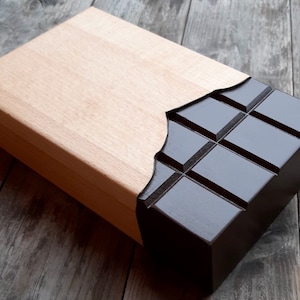 Puede incluir: Una caja de madera con un dise&ntilde;o de barra de chocolate. La caja est&aacute; hecha de madera clara y tiene un dise&ntilde;o de barra de chocolate marr&oacute;n oscuro en la parte delantera. La barra de chocolate est&aacute; dividida en cuadrados y tiene un acabado brillante.