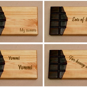 Puede incluir: Cuatro tablas de cortar de madera con un dise&ntilde;o de barra de chocolate. Las tablas est&aacute;n grabadas con el texto "My sweets", "Lots of Love", "Yummi Yummi" y "For heavy days".
