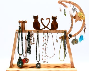 Pode incluir: Suporte de joias de madeira com um design de lua crescente, duas silhuetas de gatos e ganchos para pendurar colares e brincos. O suporte tem um acabamento de madeira natural e é decorado com uma estrela e uma pena.