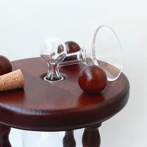 May include: A dark brown wooden hourglass with a clear glass bulb and a cork stopper. Two small wooden spheres and a clear glass funnel are also present, creating a classic and elegant design.