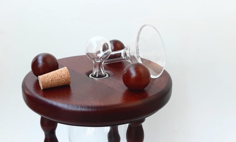 May include: A dark brown wooden hourglass with a clear glass bulb and a cork stopper. Two small wooden spheres and a clear glass funnel are also present, creating a classic and elegant design.