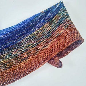 Peut inclure: Une écharpe en crochet colorée avec un dégradé de bleu, orange et marron. L'écharpe est réalisée avec un point texturé et a une bordure frangée.