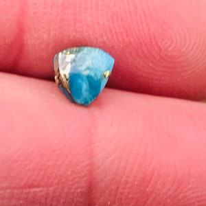 May include: A small, blue and gold gemstone with a faceted cut.