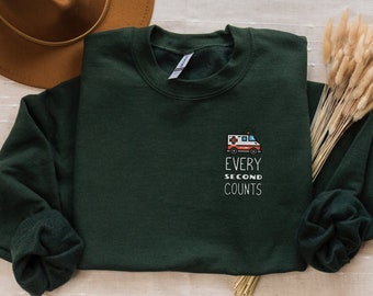 May include: A dark green sweatshirt with a white ambulance graphic and the text "Every Second Counts" on the front.