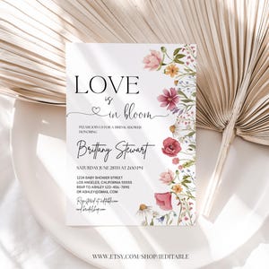 May include: A white bridal shower invitation with a floral border. The text reads "Love is in bloom" and includes the bride's name, date, time, and location. RSVP information is also included.