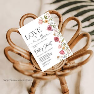 May include: A white card with a floral design and the text "LOVE is in bloom" with a heart symbol. The card is a bridal shower invitation for Britany Stewart. The invitation includes the date, time, and location of the event.